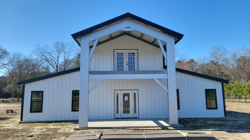 White barn-style building with black trim, two levels, clear blue sky.
