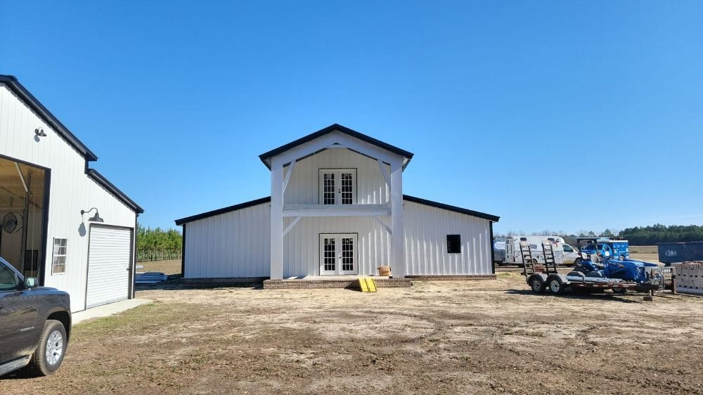 White barn-style building with black trim, and a second building to the left, under a blue sky.