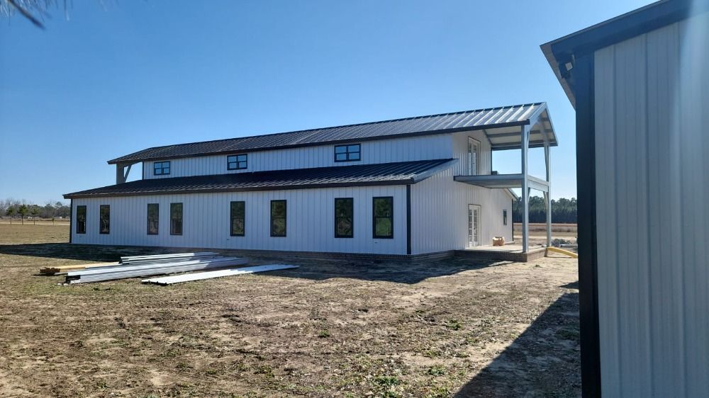White two-story barn with black roof and trim on a sunny day.