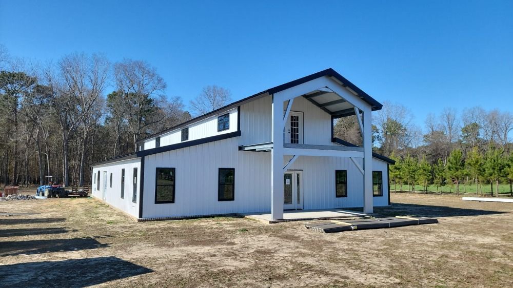 White barn-style building with black trim, balcony, and clear blue sky.