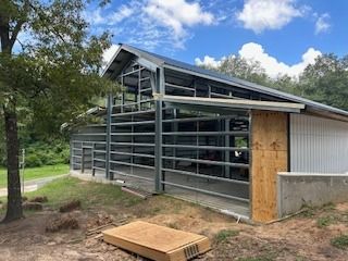 Metal frame barn under construction with gray roof and white siding; outdoor setting.