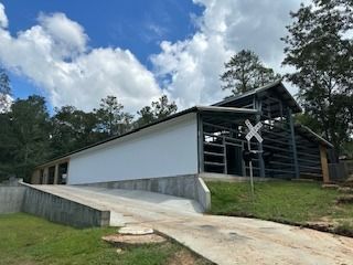 Building with a white wall and metal frame with a sloped concrete driveway on a sunny day.