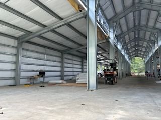 Interior of a large metal building under construction, with steel beams, concrete floor, and insulated walls.