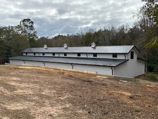 White barn with black roof, vents, and trim; set in a clearing, under cloudy sky.