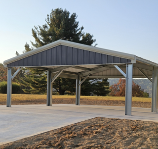 Carport with metal frame and roof, on a concrete pad, surrounded by grass and trees.