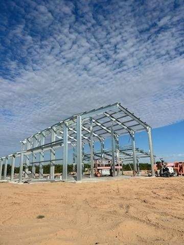 Steel frame of a building under construction on a dirt lot, blue sky with clouds in the background.