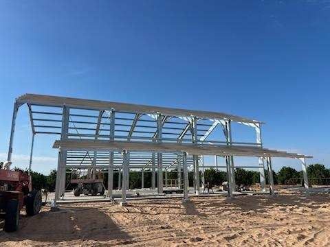 Steel frame of a two-story building under construction on a dirt lot, against a clear blue sky.