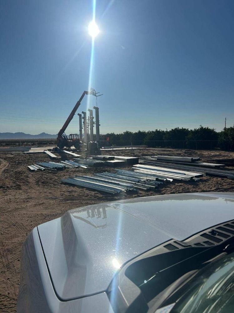 Construction site with crane lifting metal beams under a bright sun. Ground scattered with metal sheets.