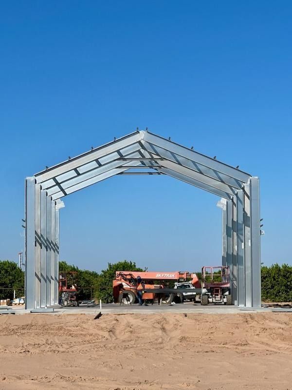 Steel frame of a building under construction, open on two sides, with equipment inside, against a blue sky.