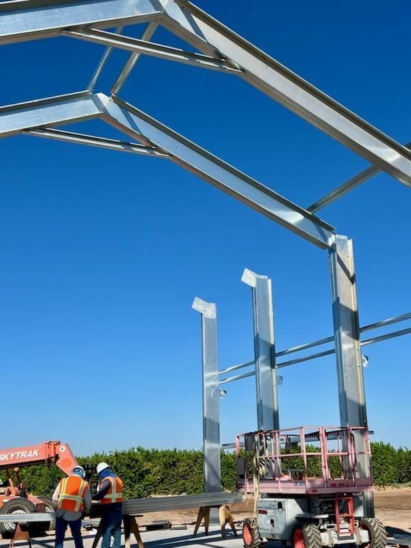 Steel frame construction against a blue sky, with workers and lift equipment.