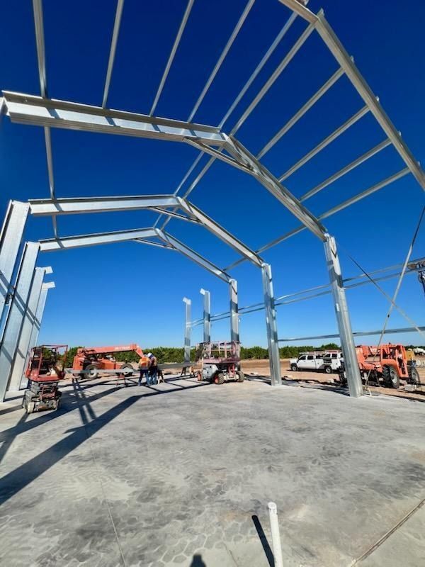 Steel frame of a building under construction, on a concrete slab, with workers and construction equipment.