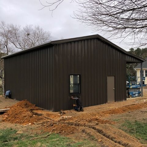 Brown metal building with two workers outside, cloudy sky.