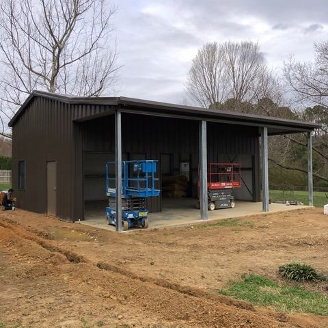 Brown metal shed with a covered carport, two lifts inside, and trenches in front.