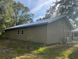 Tan metal building with white trim, a silver roof, and two windows on a grassy lot.