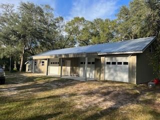 Tan building with garage doors, covered porch, and metal roof, in a wooded area.