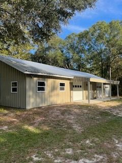 Tan metal building with a white garage door, and a porch. Green trees and blue sky background.