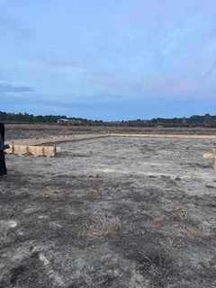 Construction site with wooden foundation outline in a field under a cloudy sky.
