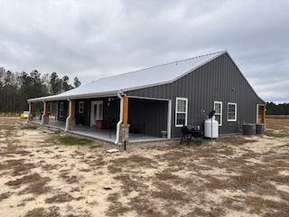Gray metal-sided house with a porch and silver roof on a dry, grassy lot under a cloudy sky.