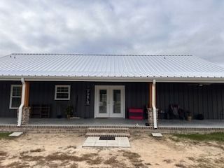 A house with a white metal roof and dark gray siding under a cloudy sky.