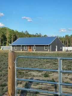 Gray building with blue roof in a rural setting, visible behind a metal fence and wooden post.
