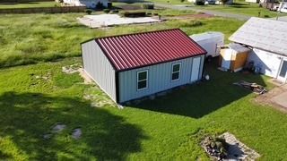 Metal shed with red roof, two windows, and door, next to a house on a grassy lawn.