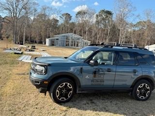 Blue SUV parked in a grassy field with a greenhouse in the background.