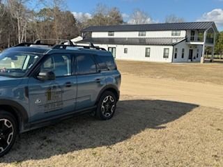 Blue SUV parked in front of a two-story white barn-style building with a black roof.