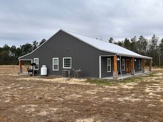 Gray metal-clad barn-style house with a white roof and porch, set in a field.