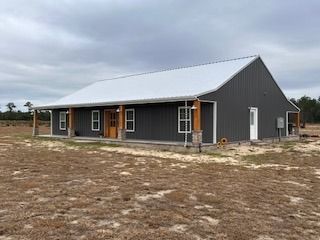 Gray metal-sided house with a white roof and porch, set in a field under a cloudy sky.
