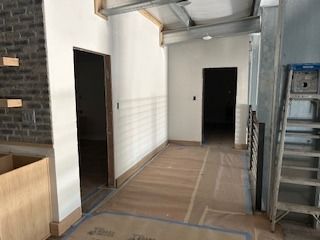 Interior hallway with two doorways and a brick wall. A ladder leans against a metal structure.