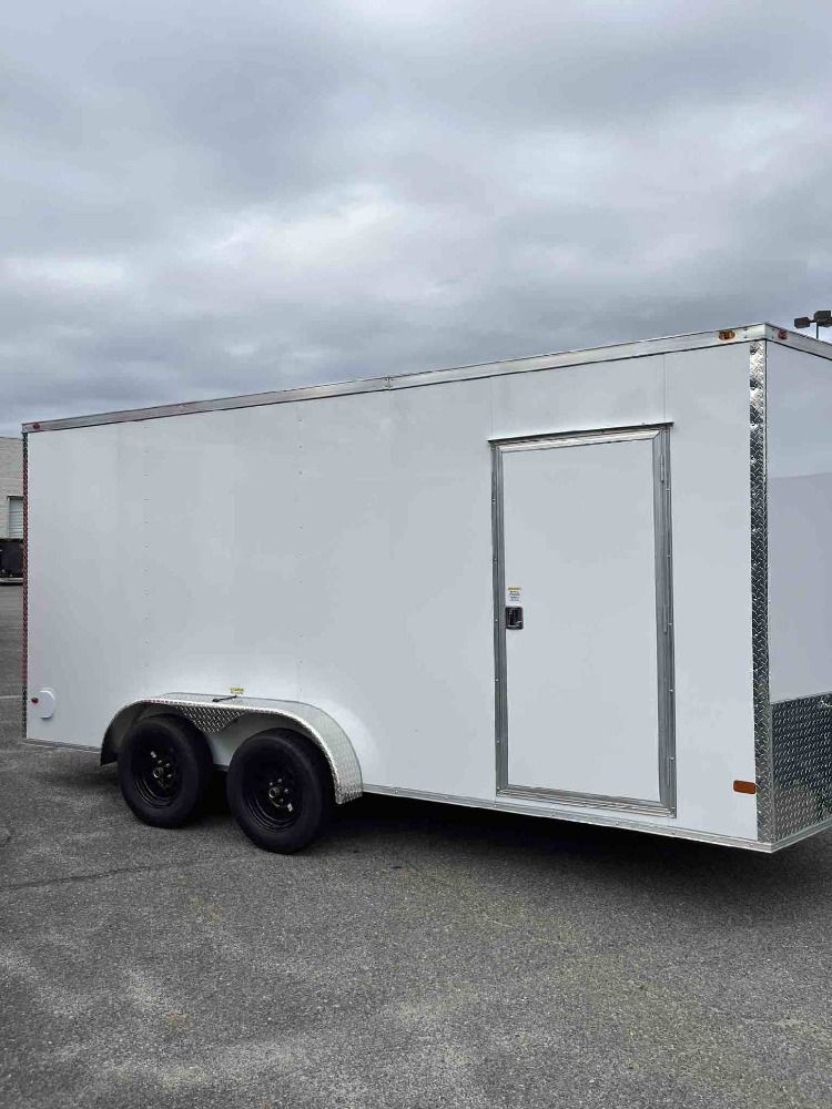 White enclosed cargo trailer with black wheels and a side door parked outdoors on a cloudy day.