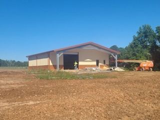 A tan and brown metal building under construction with a clear blue sky. An orange lift stands nearby.