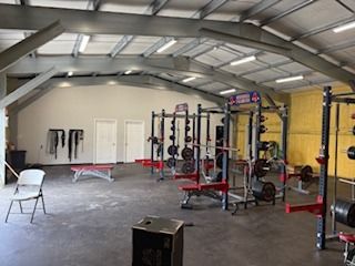 Weightlifting gym interior with squat racks, benches, weights, and metal beams.