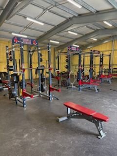 Weightlifting gym with red and black squat racks and a bench.