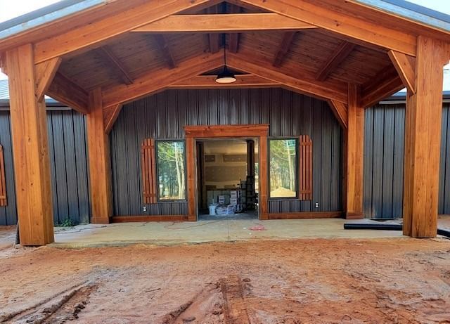 Wooden-framed building with brown siding and porch. Open doorway and windows. Sandy ground.