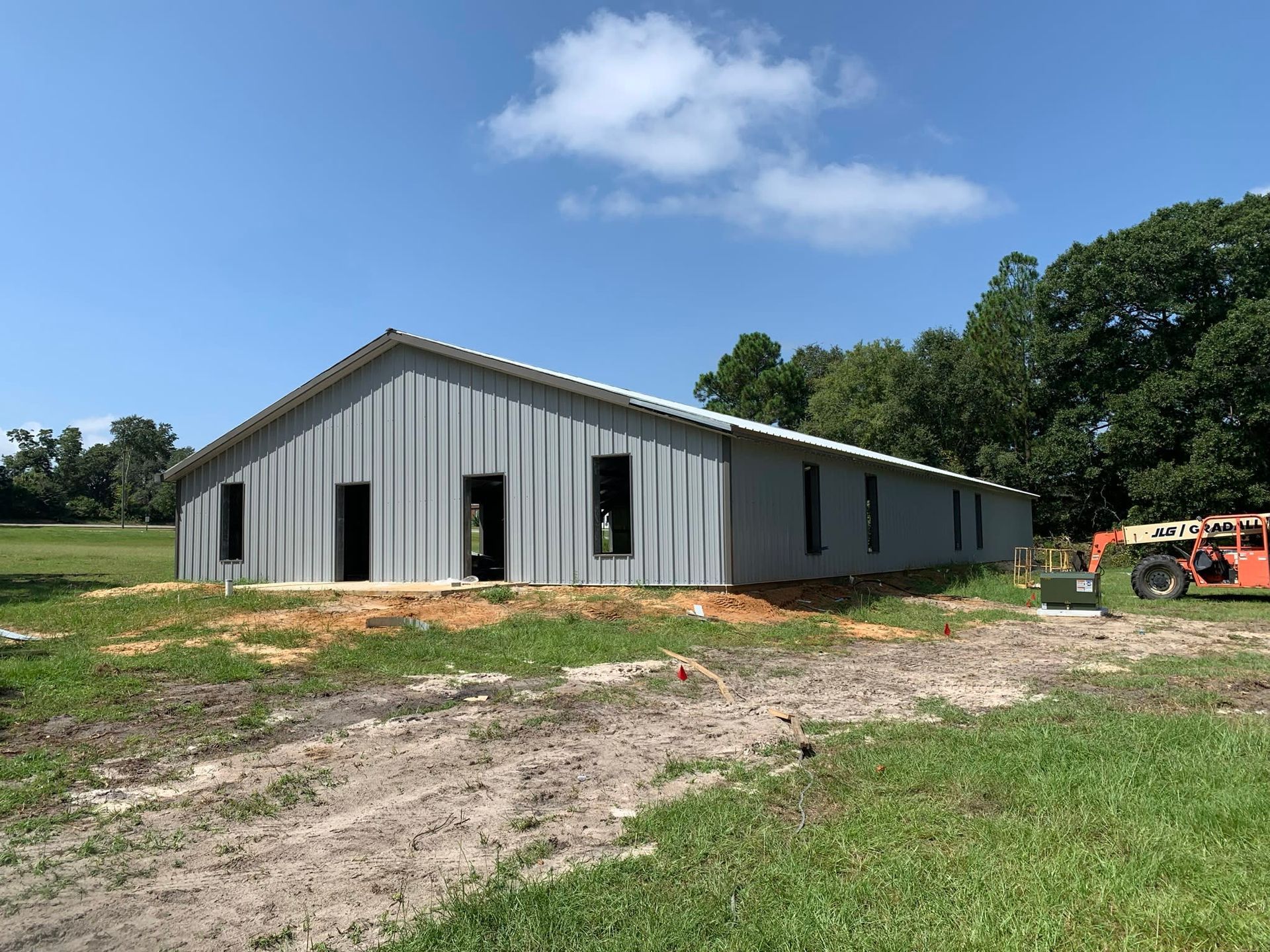 A gray metal building under construction on a grassy lot