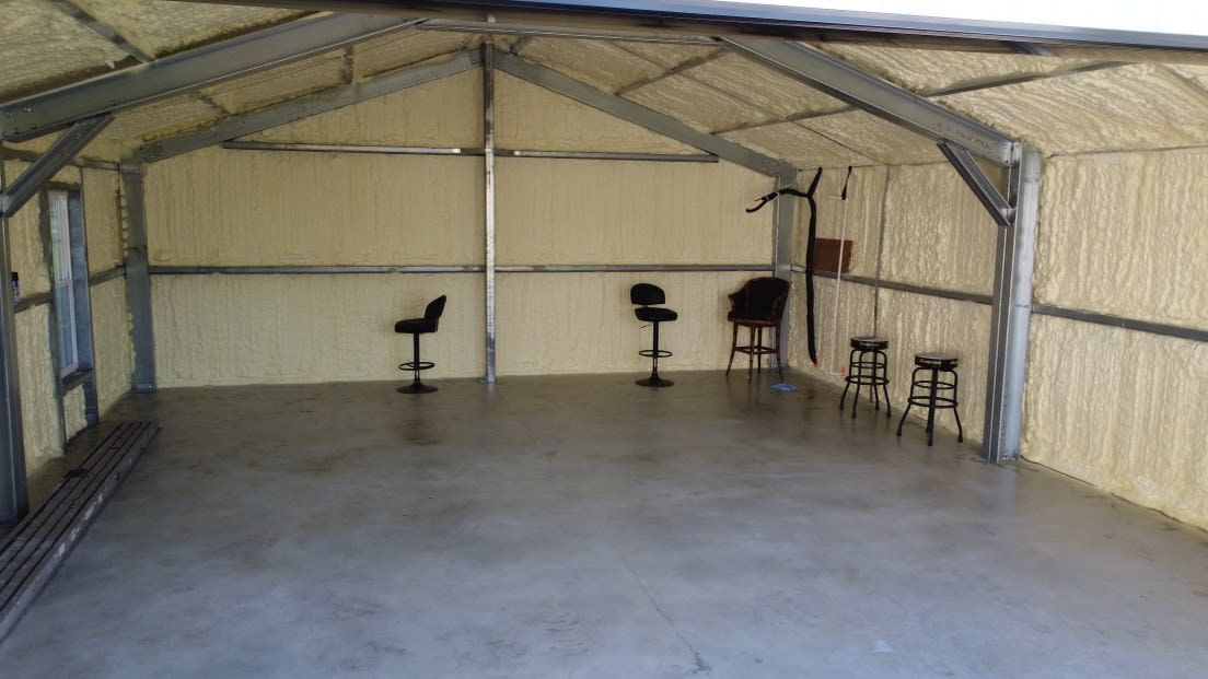 Interior of a metal building with spray foam insulation, concrete floor, and stools