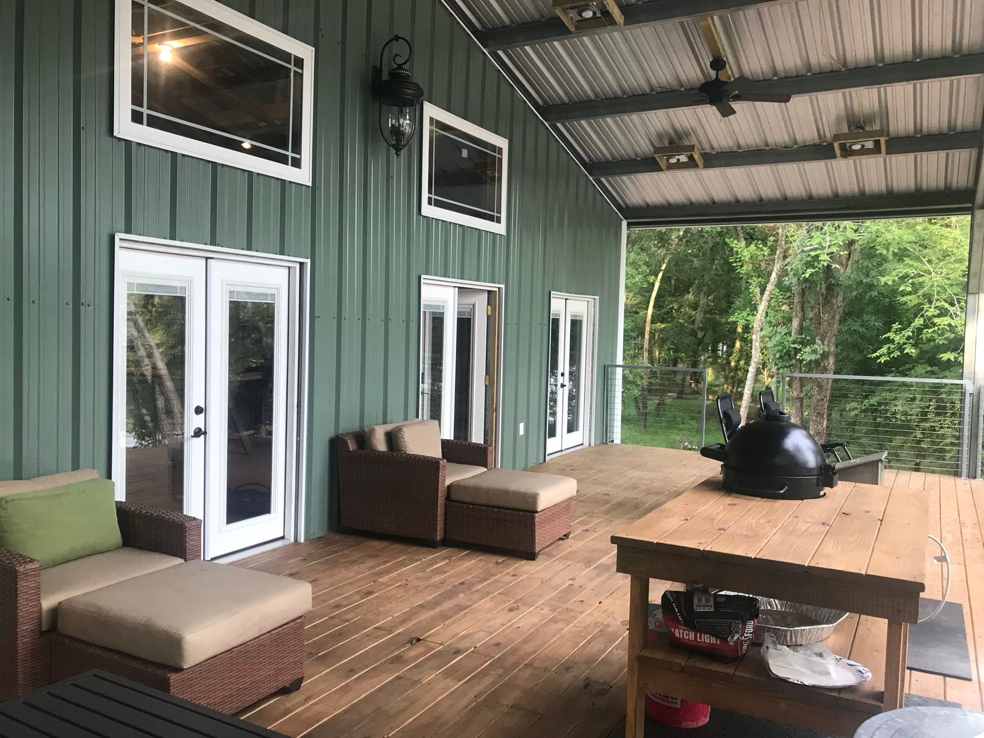 Covered porch with green metal siding, glass doors, brown deck, and outdoor furniture
