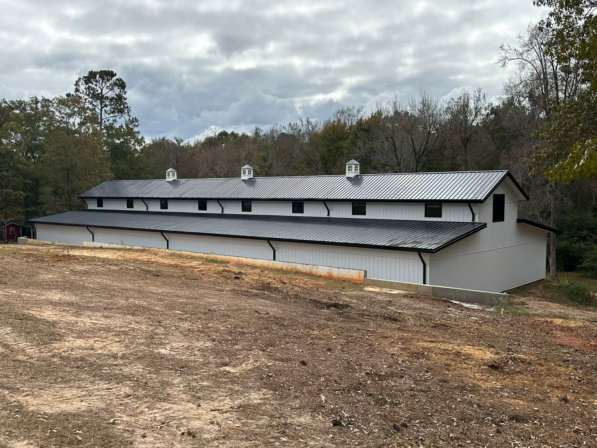 White barn with black roof and trim against a backdrop of trees and a cloudy sky