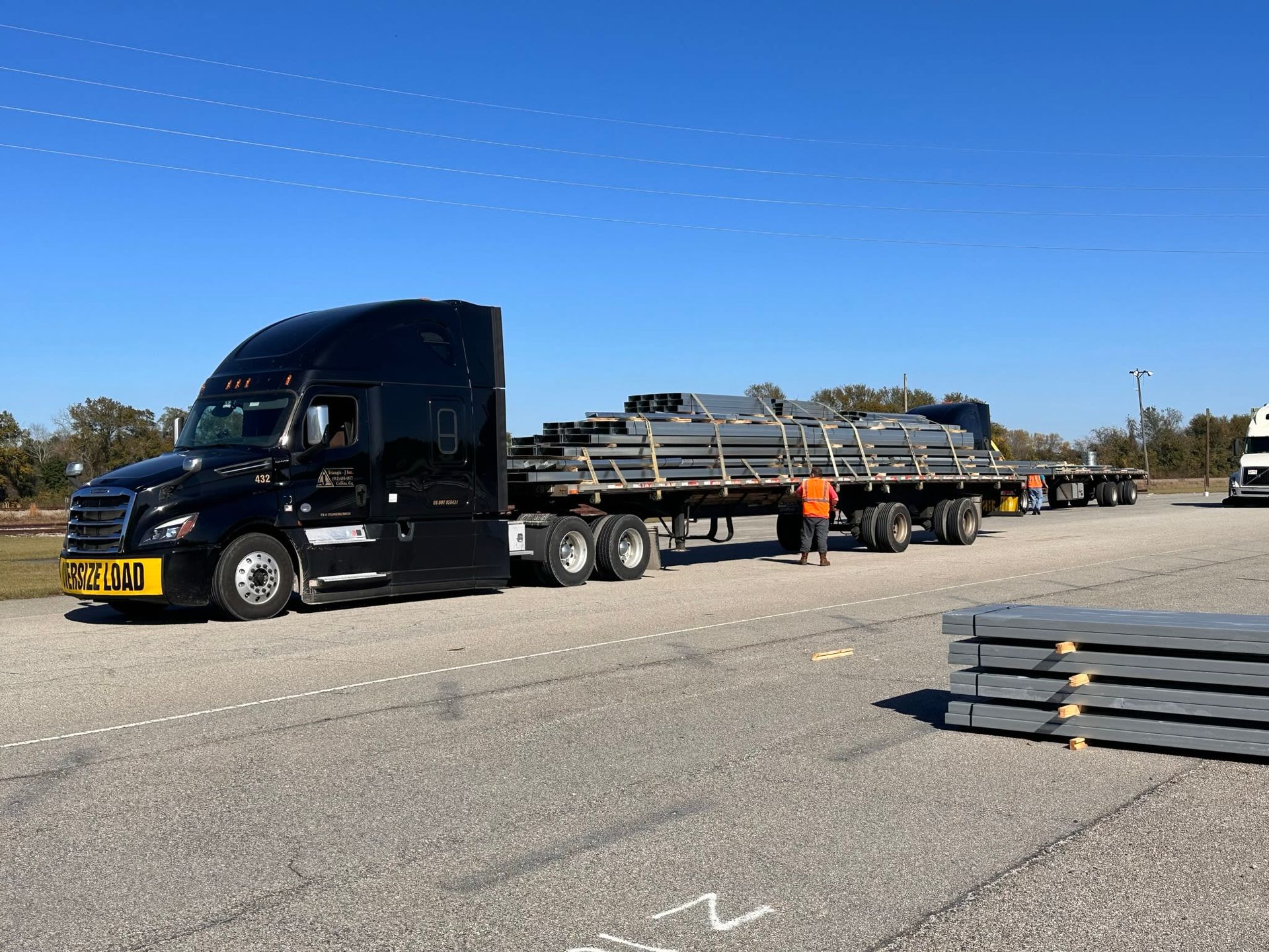 Black semi-truck hauling gray metal sheets on a flatbed trailer