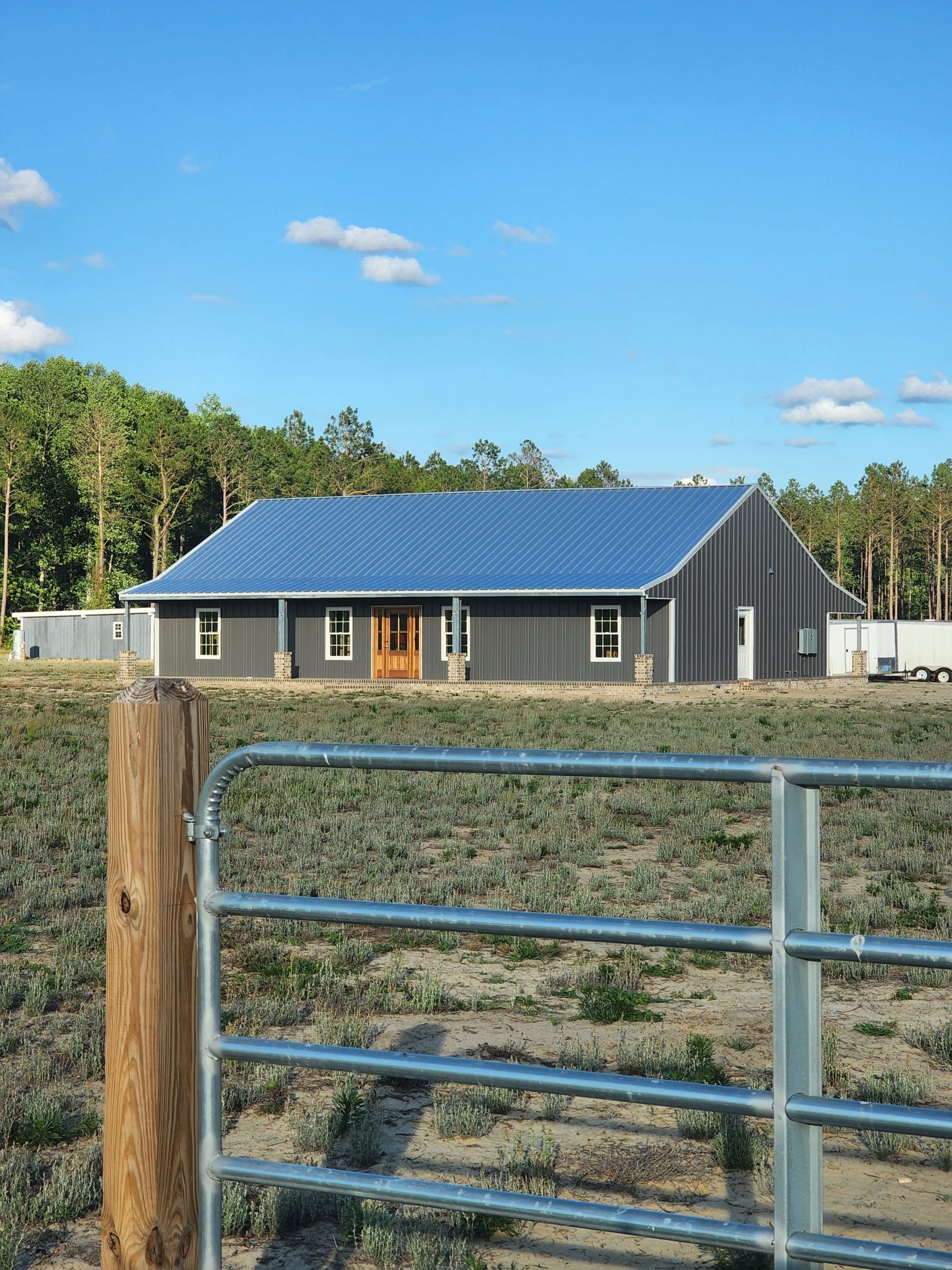 Gray house with solar panel roof, wooden door, set behind a metal gate with a blue sky backdrop