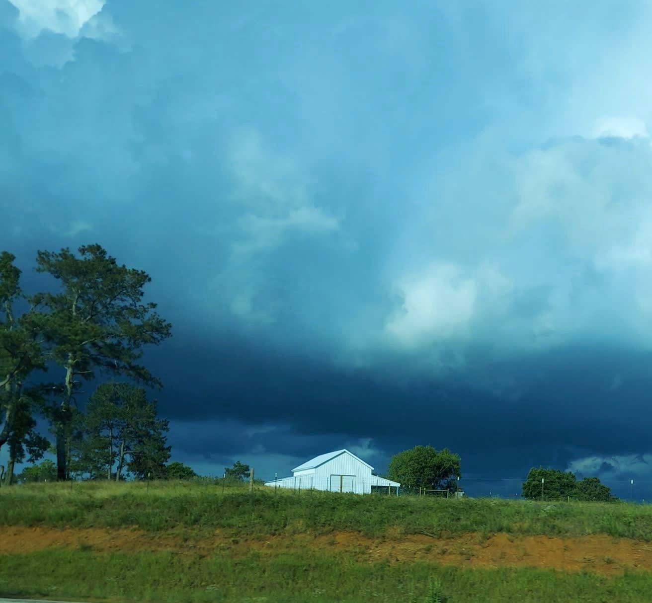 Dark, stormy clouds loom over a white house and trees on a green hillside