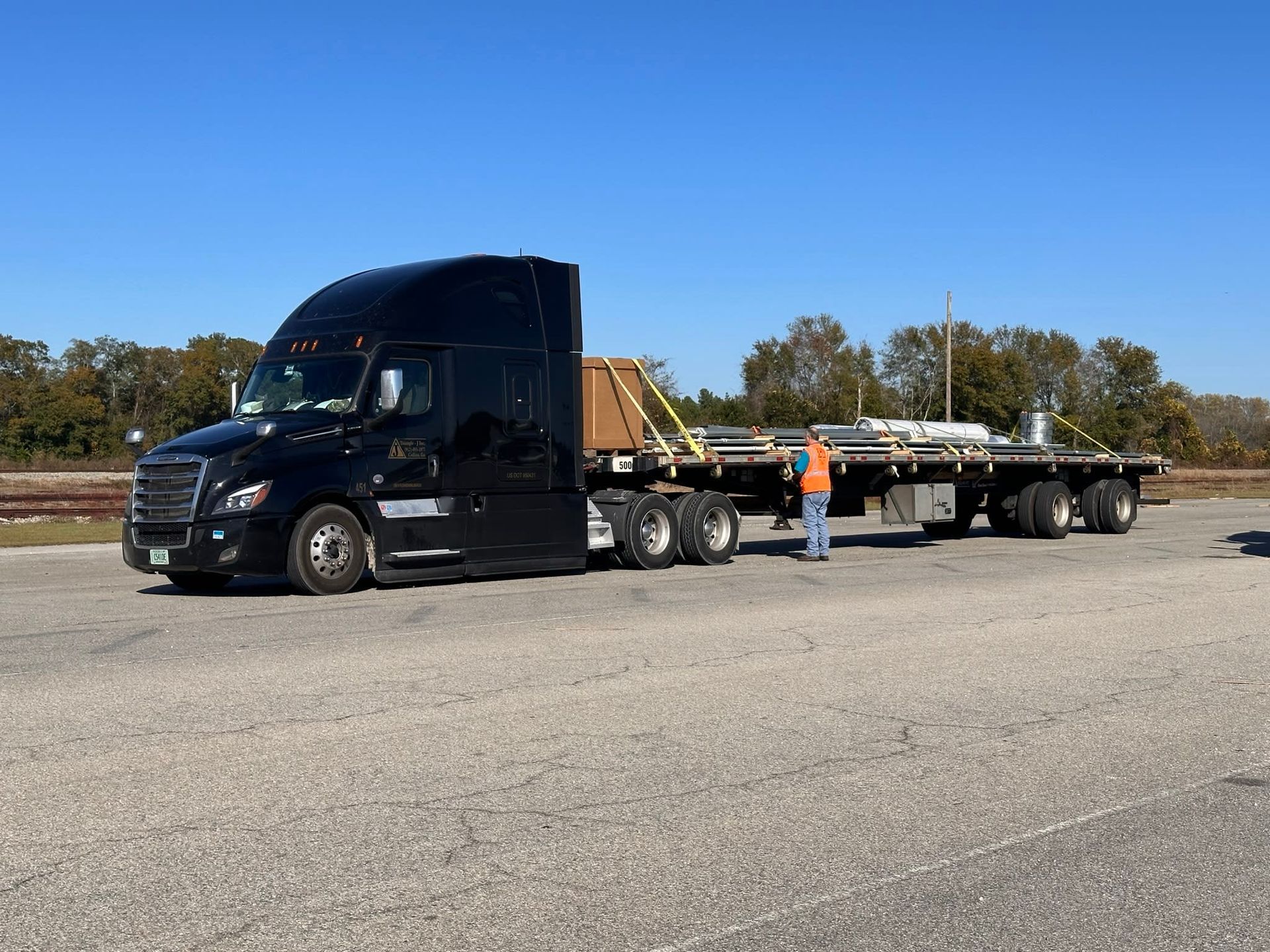 Black semi-truck with flatbed trailer, transporting materials