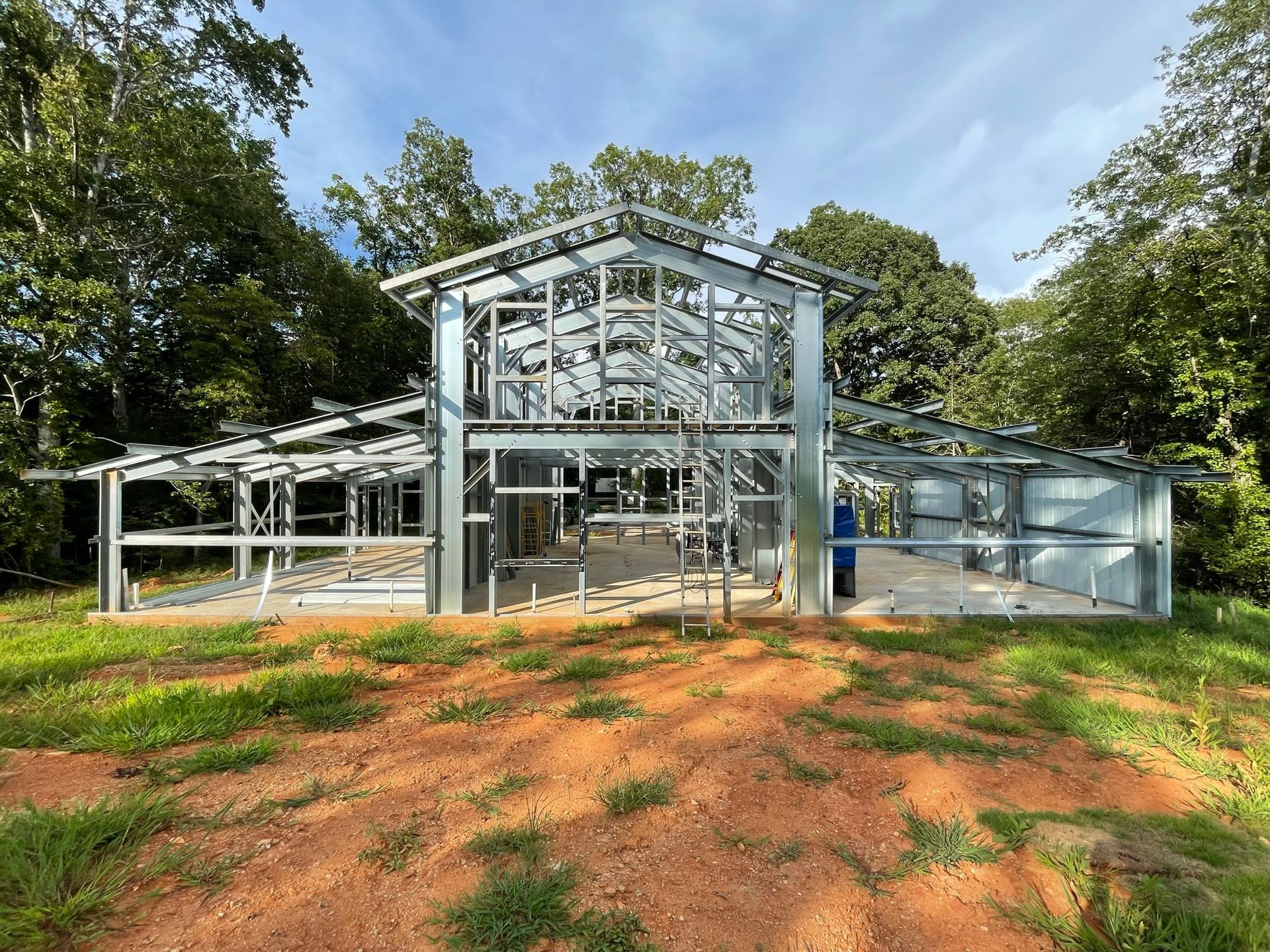 Metal framework of a two-story building under construction, set in a grassy area with trees