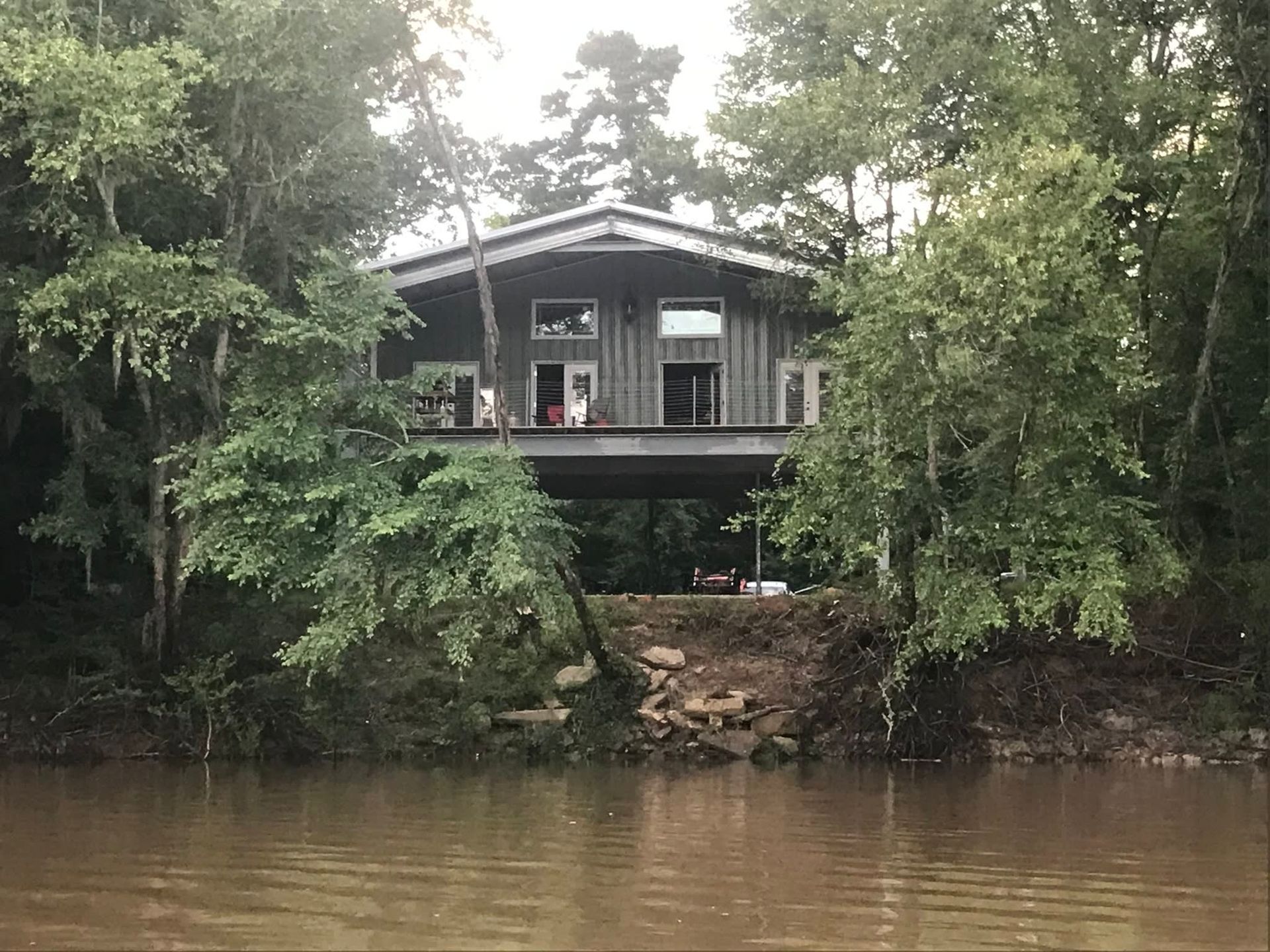 House on stilts over muddy water, surrounded by trees