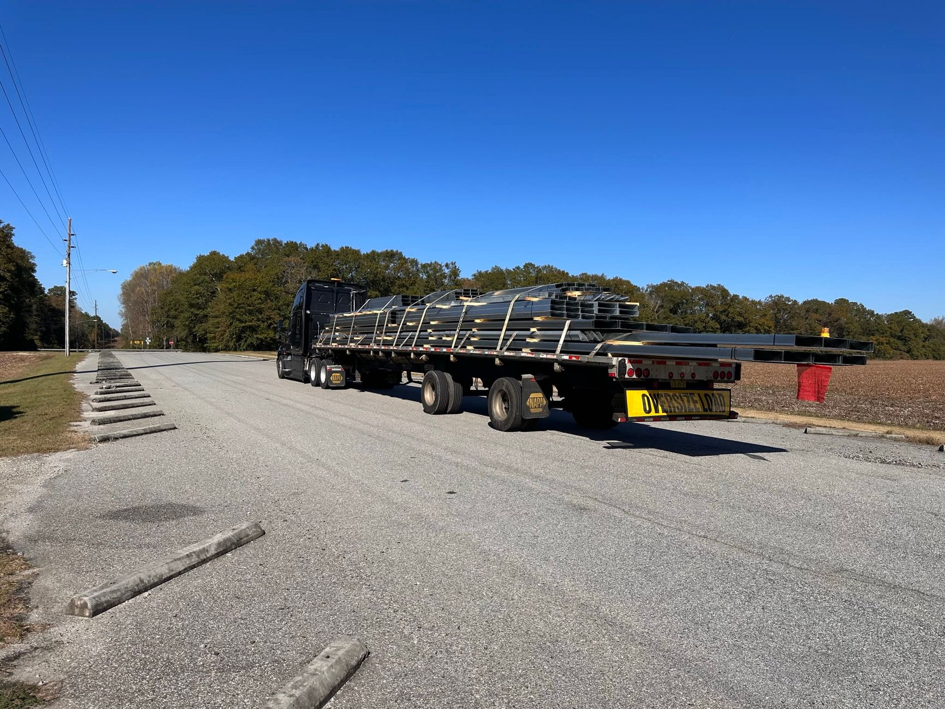 A flatbed truck with metal beams on a gravel road under a clear blue sky
