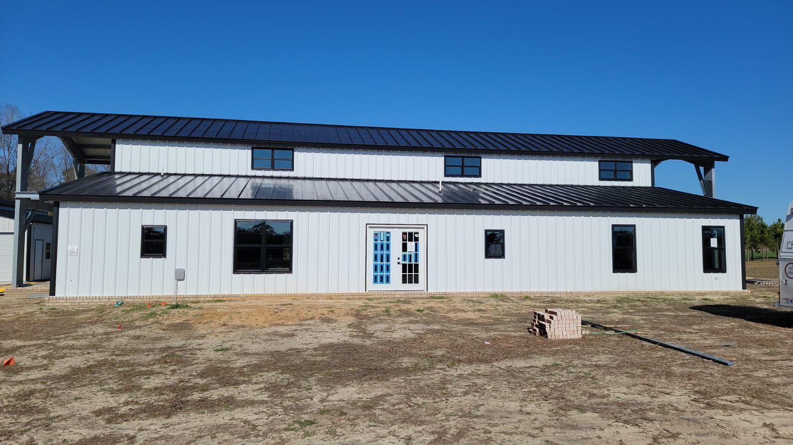 Two-story white building with black metal roof and windows against a clear blue sky