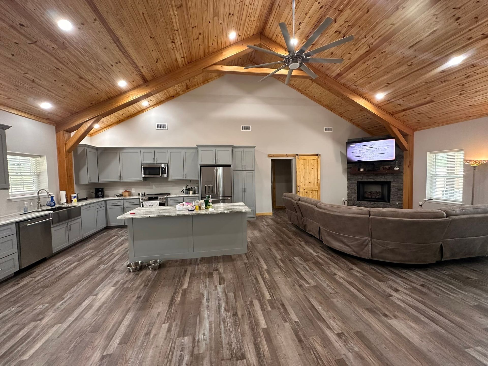 Spacious open-plan kitchen and living area with wood beams, gray cabinets, and large gray sectional