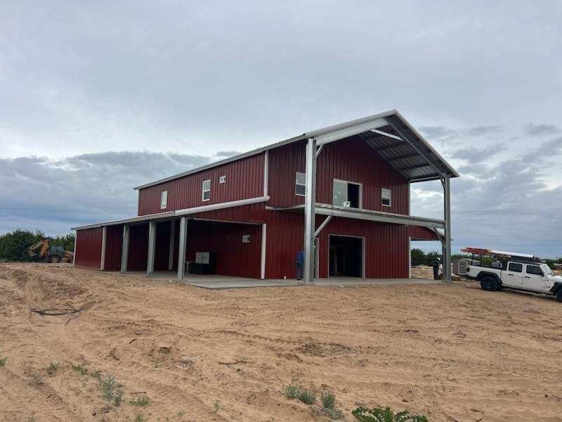 Red barn-style building under construction; overcast sky, open area, concrete foundation.
