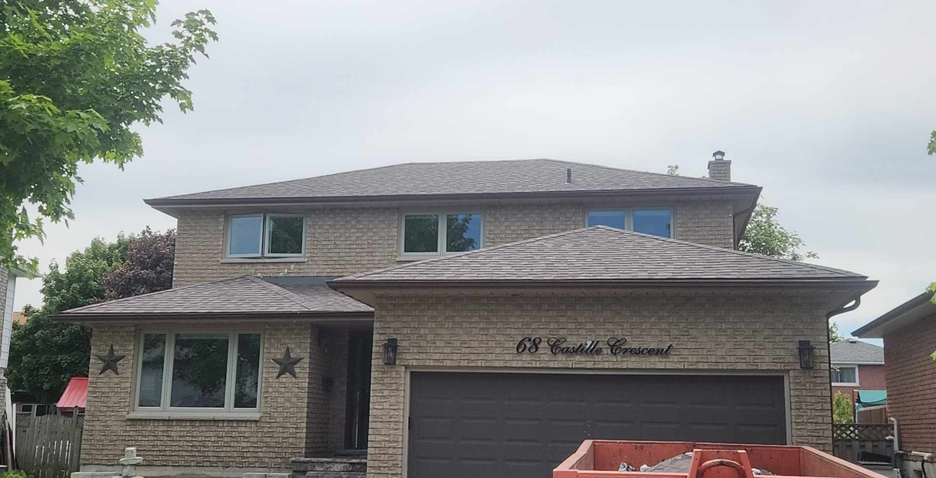 A large brick house with a large garage and a dumpster in front of it.